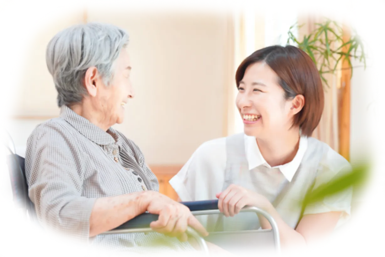 車椅子に座った高齢女性と介護士の女性が笑顔で会話している様子